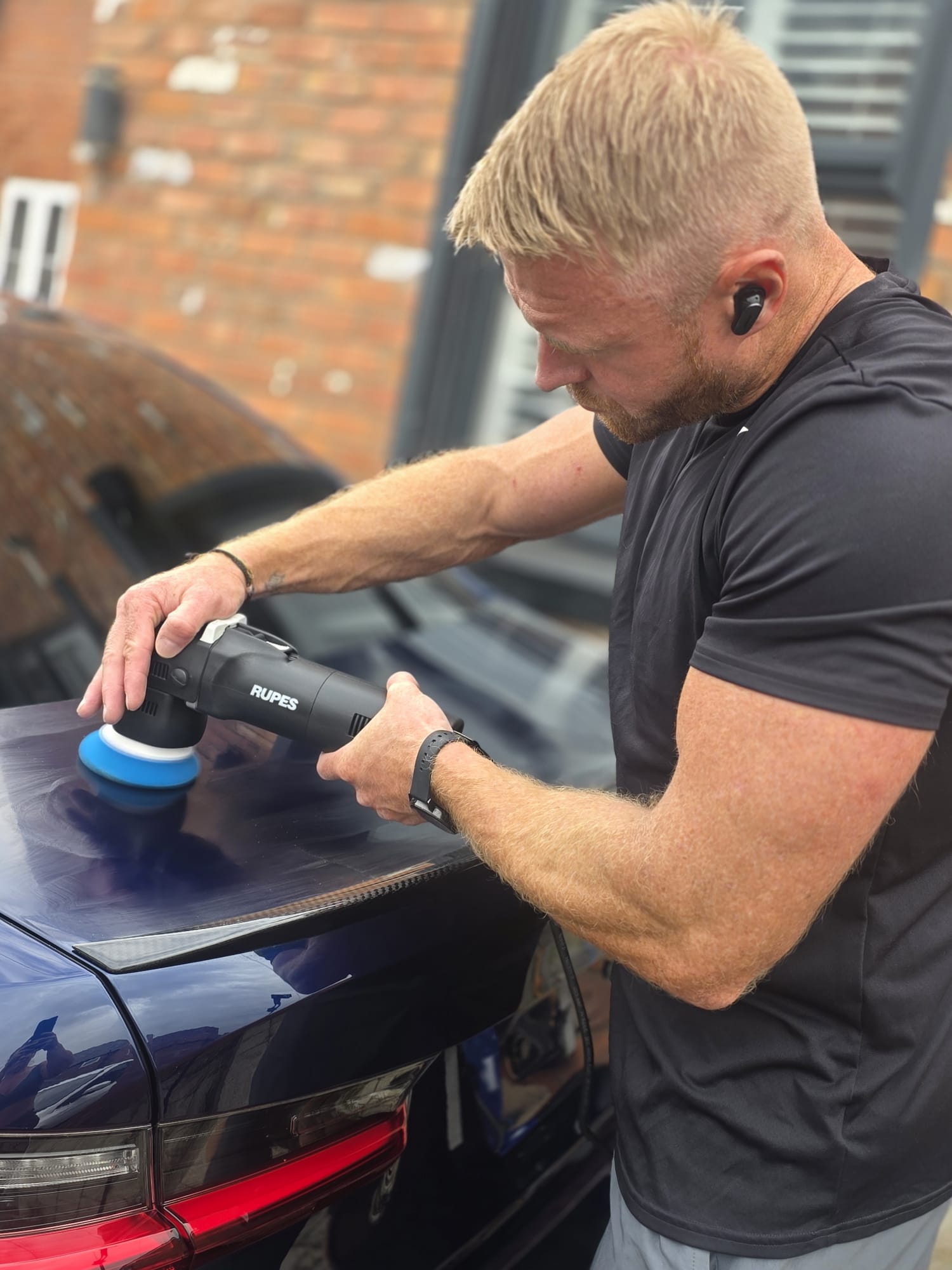 Carbon Detailing technician machine polishing a dark car bonnet with a RUPES polisher